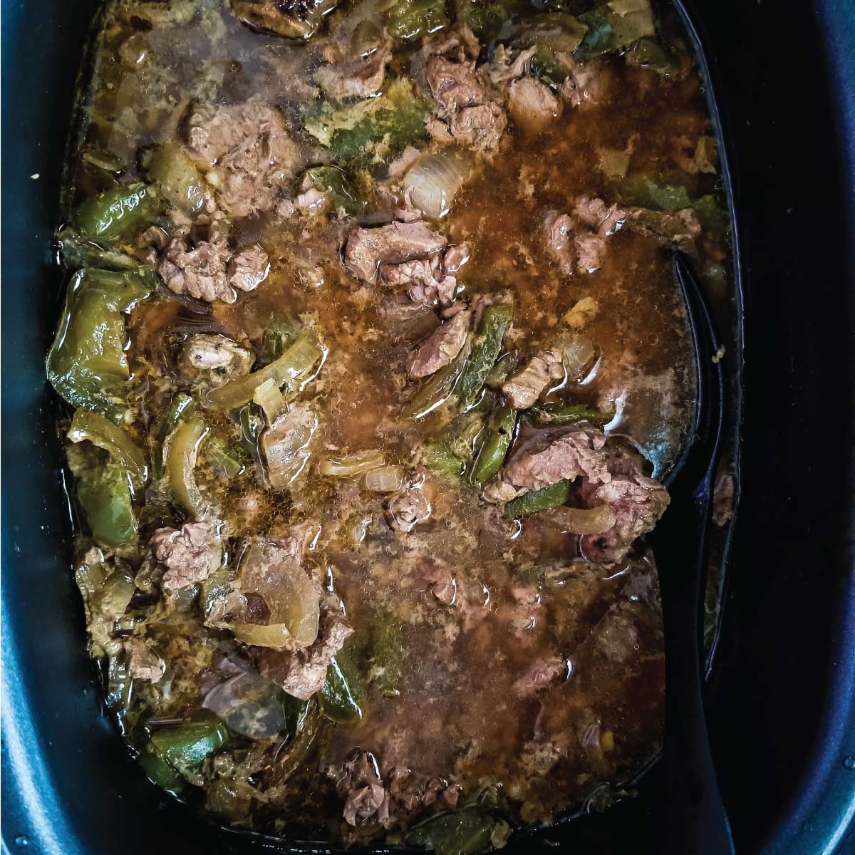 Beef, peppers, onions, seasoning and broth in the slow cooker just after cooking and ready to put on rolls.