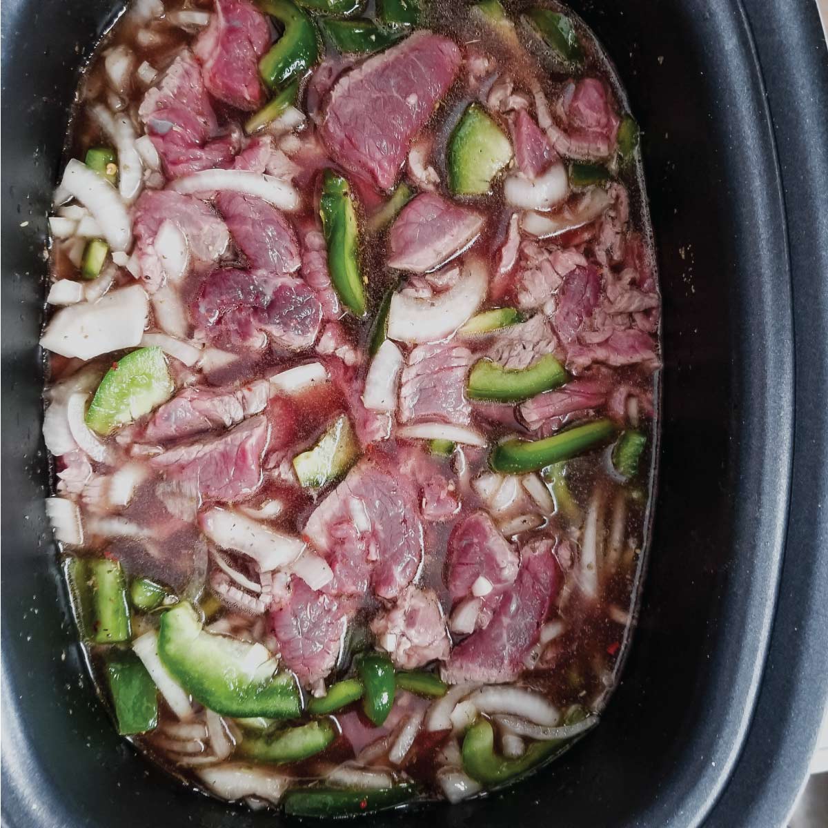 Beef, peppers, onions, seasoning and broth in the slow cooker just before cooking.