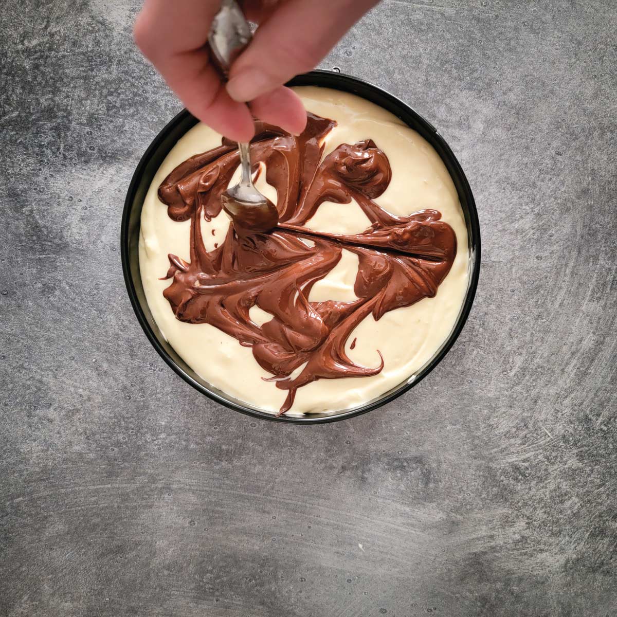 Cheesecake batter in the springform pan with chocolate being swirled around on the top.