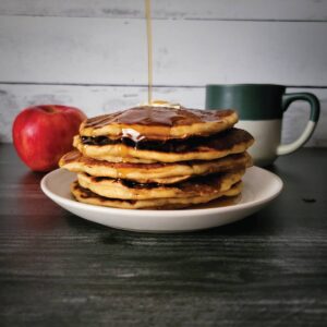 Pancakes stacked on a plate with maple syrup being poured over top.