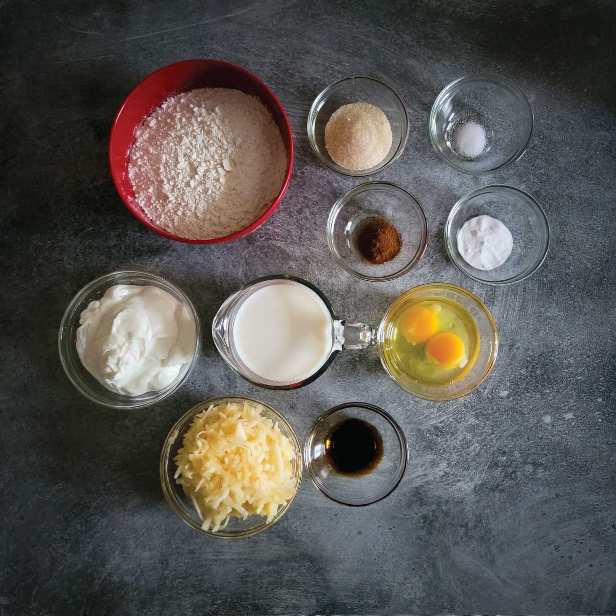 Ingredients for apple pancakes prepped - flour, sugar, salt, baking soda, cinnamon, eggs, milk, yogurt, vanilla extract and shredded apple.