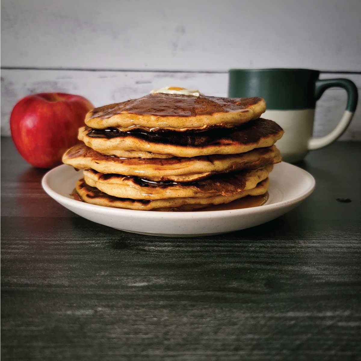 Apple pancakes on a plate with a slice of butter on top and maple syrup over the top.