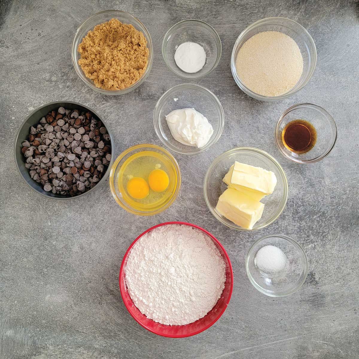 Cookie ingredients prepped - flour, salt, butter, eggs, chocolate chips, yogurt, vanilla extract, sugar, baking soda and brown sugar.