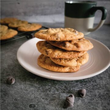 Cookies stacked on a small serving plate with chocolate chips scattered for decoration and a cup of coffee by the cookies.