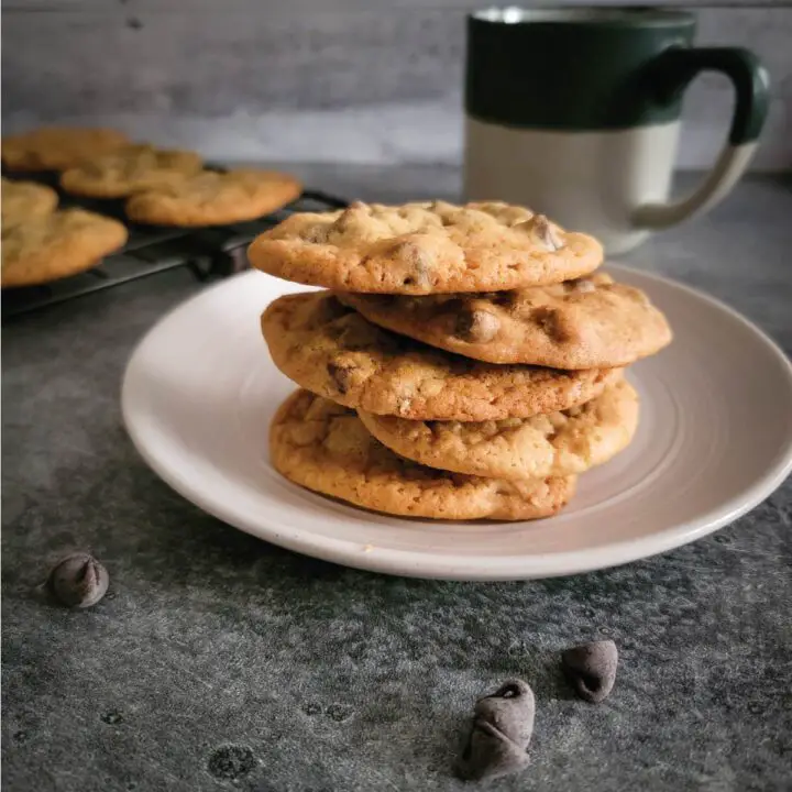 Cookies stacked on a small serving plate with chocolate chips scattered for decoration and a cup of coffee by the cookies.