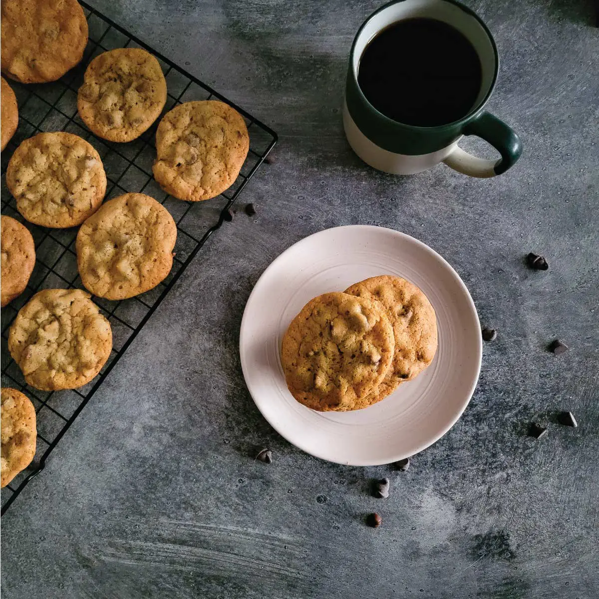 Cookies on a small plate and some on a cooling rack with a cup of coffee by the cookies.