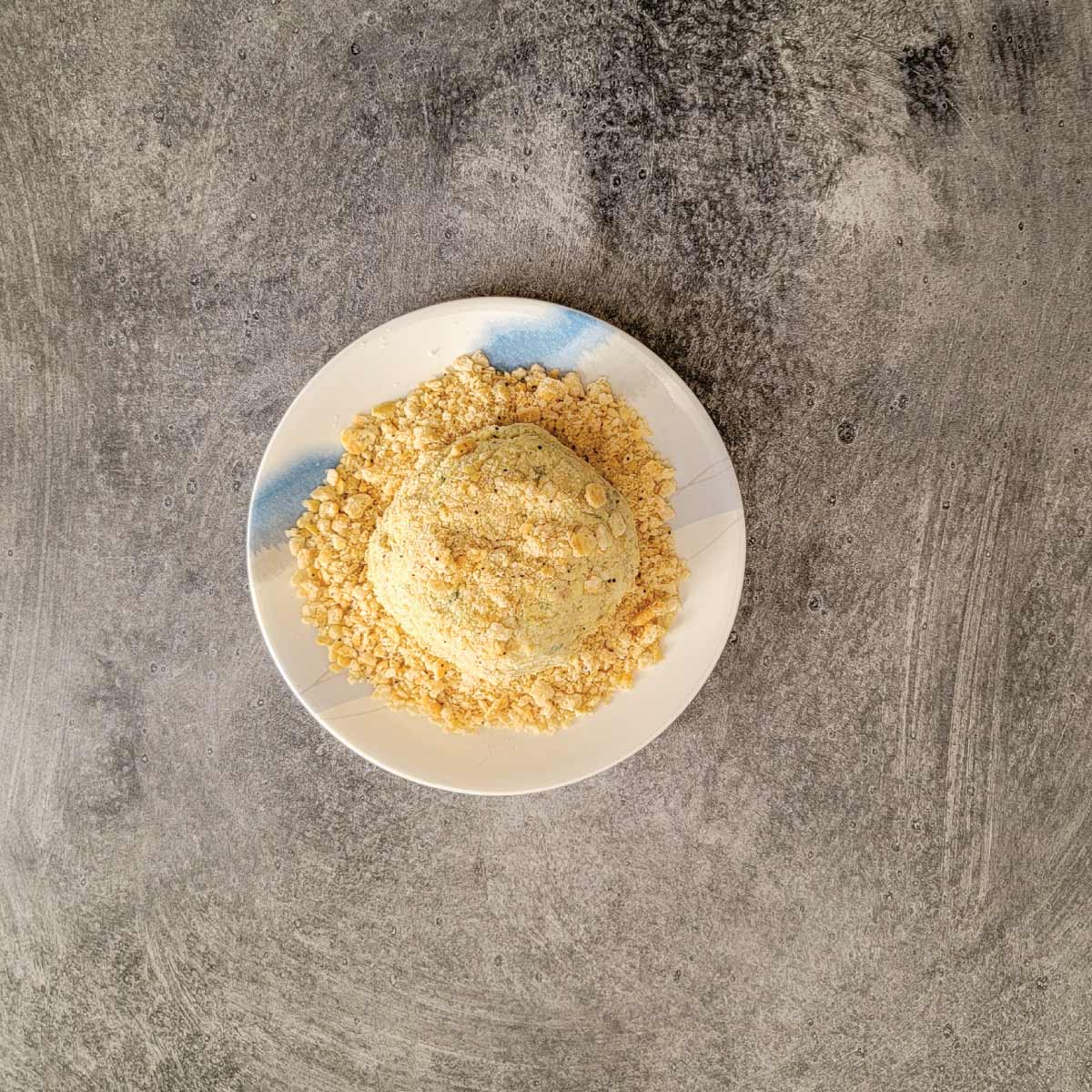 Cheeseball being coated in crushed crackers on a small plate.