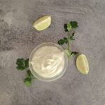 Sour cream mixed with lime and cilantro in a small bowl with lime quarters and fresh cilantro around the bowl for decoration.