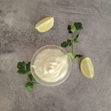 Sour cream mixed with lime and cilantro in a small bowl with lime quarters and fresh cilantro around the bowl for decoration.