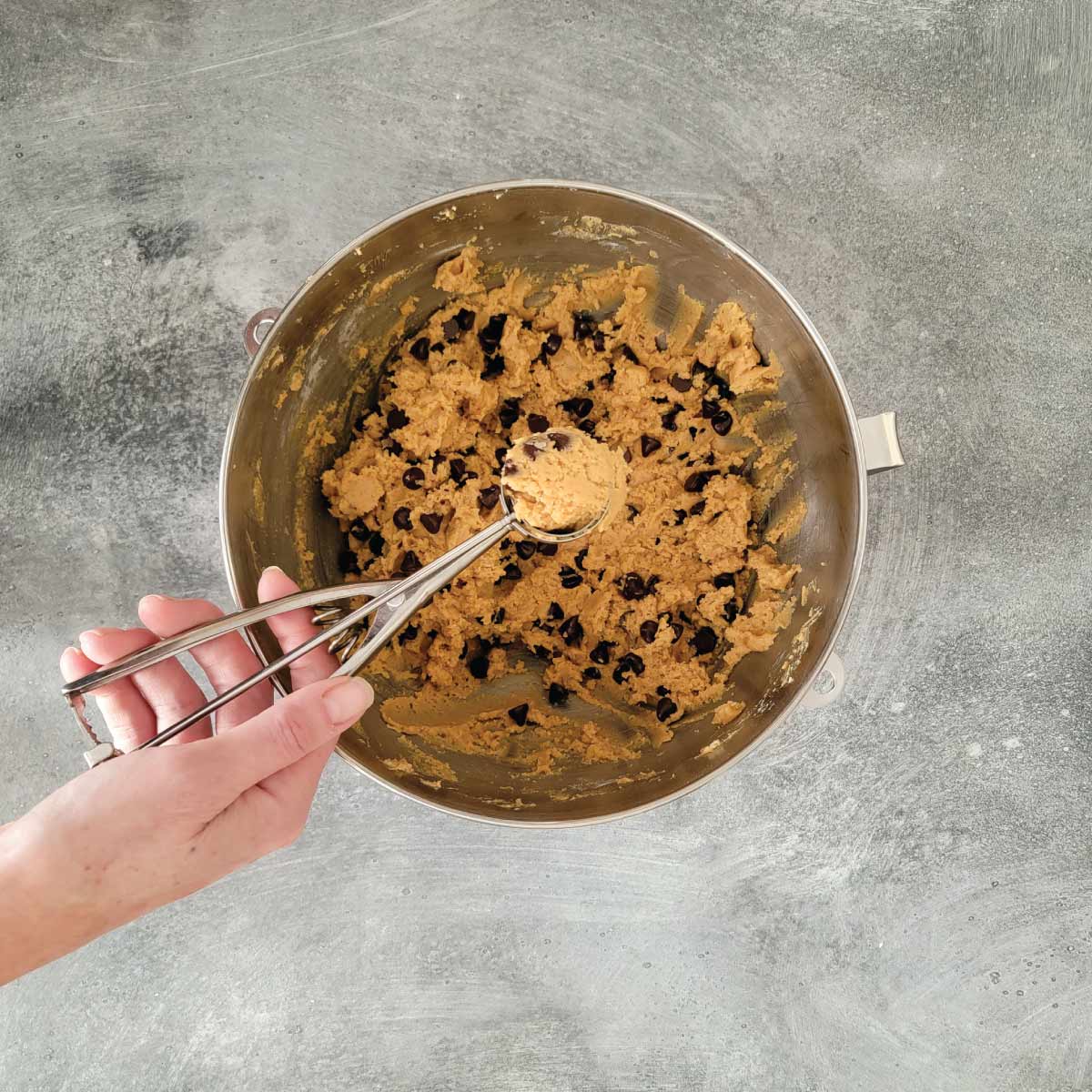 Cookie dough in a mixing bowl with a cookie scoop being used to scoop dough into balls.