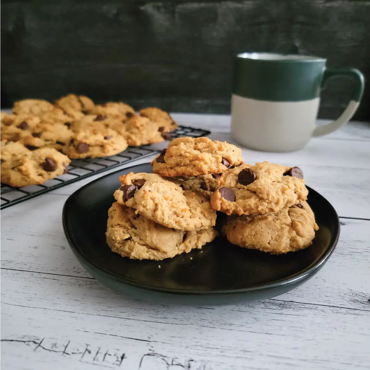 Cookies on a small plate and some on a cooling rack with a cup of coffee by the cookies.