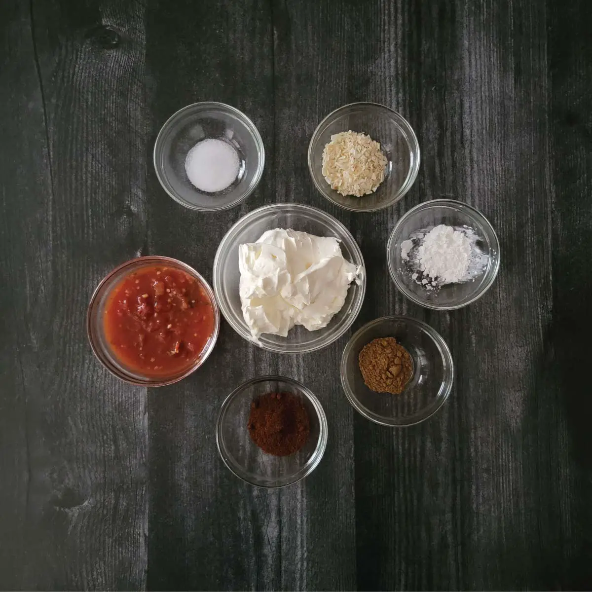 Taco dip ingredients in prep bowls - salt, minced dried onion, cornstarch, sour cream, salsa, chili powder and cumin.