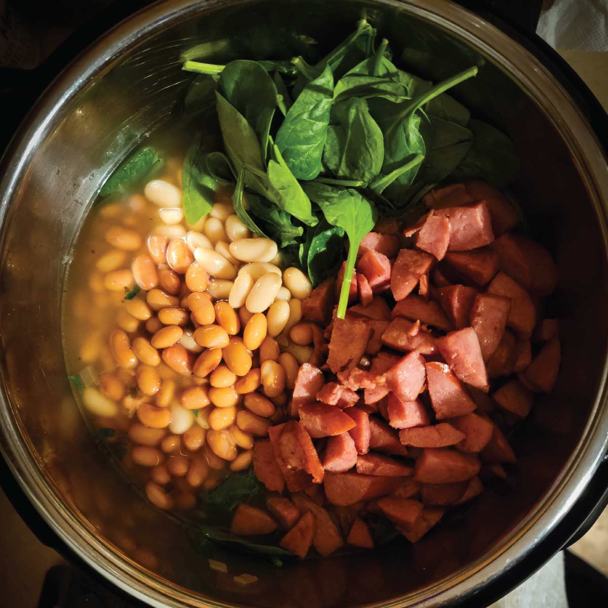 Soup in the Instant Pot with the beans, kielbasa and spinach on top ready to mix in.