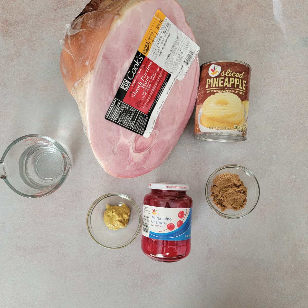 Ingredients for making ham and the ham glaze - water, mustard, cherries, brown sugar, pineapple slices and a shank portion ham.