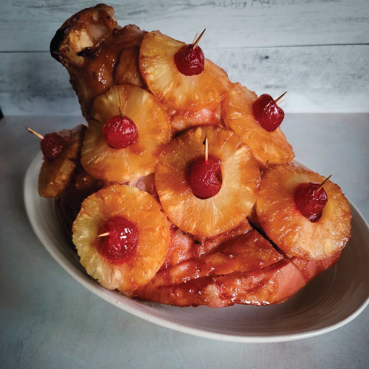 Ham with pineapple slices and cherries on it sitting on a platter resting before cutting.