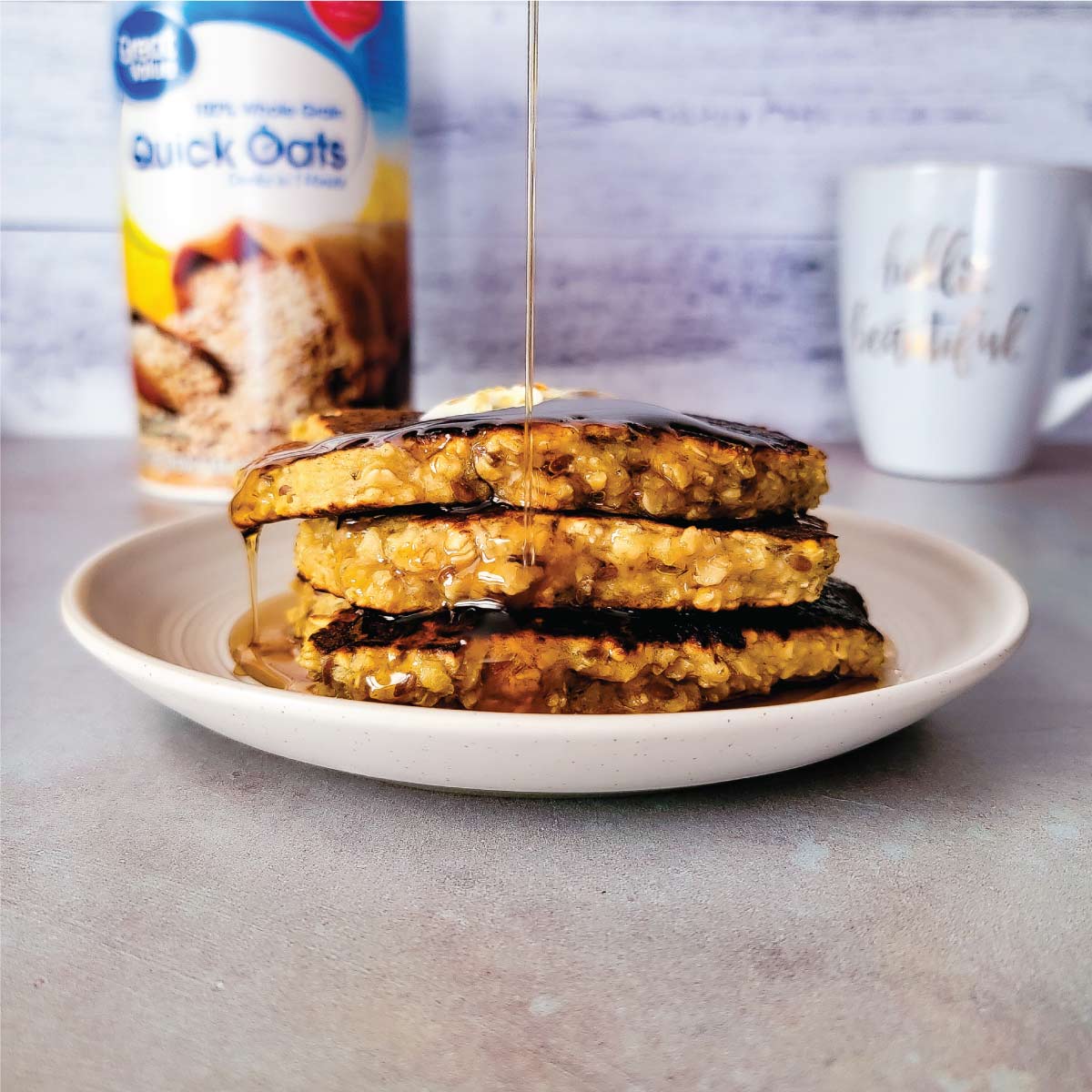 Pancakes stacked on a small serving plate with maple syrup being poured over top.