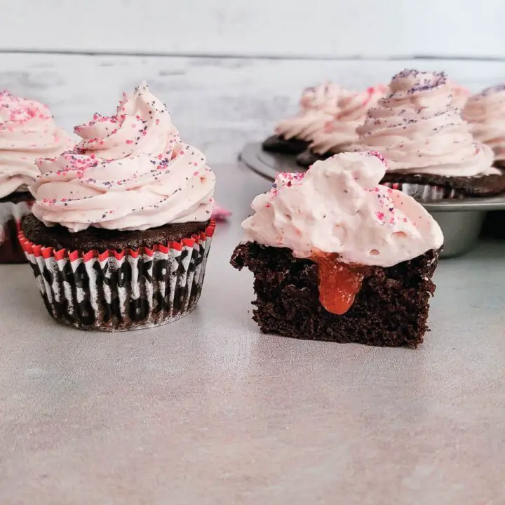 Chocolate cupcakes with one cut in half to show strawberry filling in the inside.