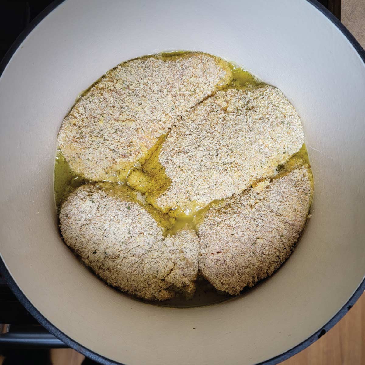 Breaded chicken frying in olive oil in a Dutch oven.