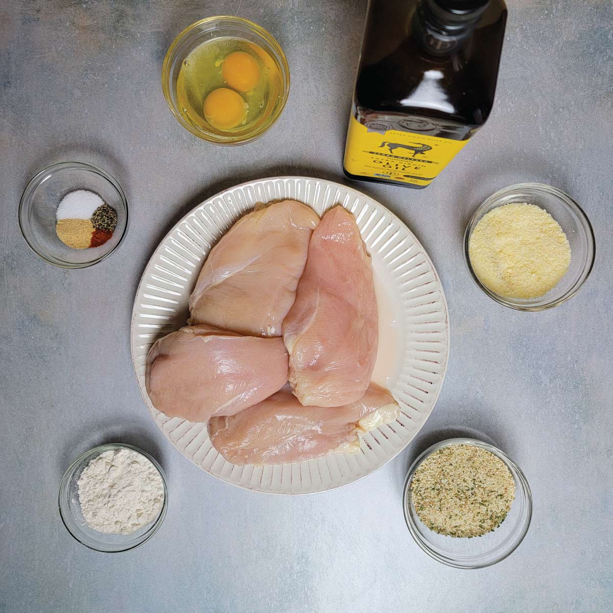 Ingredients for making the fried chicken prepped - flour, bread crumbs, chicken breasts, parmesan cheese, olive oil, eggs, salt, garlic, pepper and cayenne pepper.