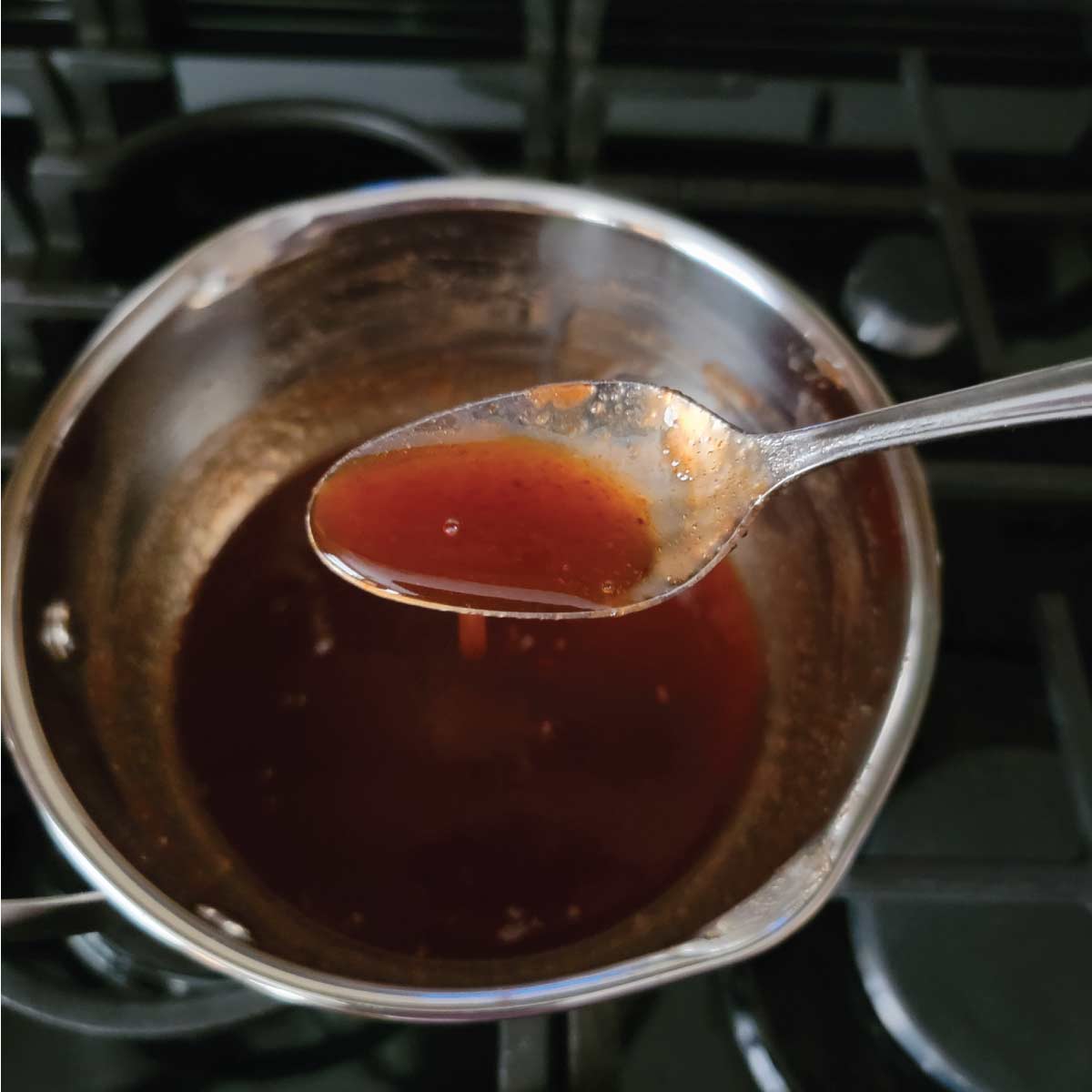 Spoon scooping some glaze out of a pot to show the thickened consistency.