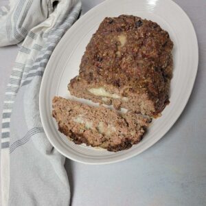 Meatloaf stuffed with cheese on a platter with a slice cut off to show the cheese inside.