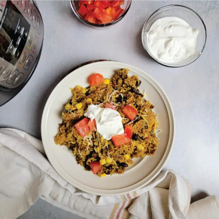 Taco rice in a serving dish topped with cheese, sour cream and tomatoes.