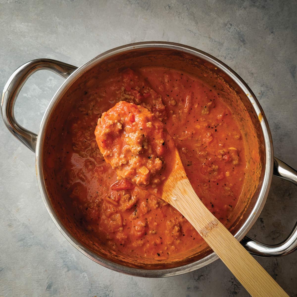 Vodka sauce with sausage in a sauce pot after cooking being spooned out of the pot.