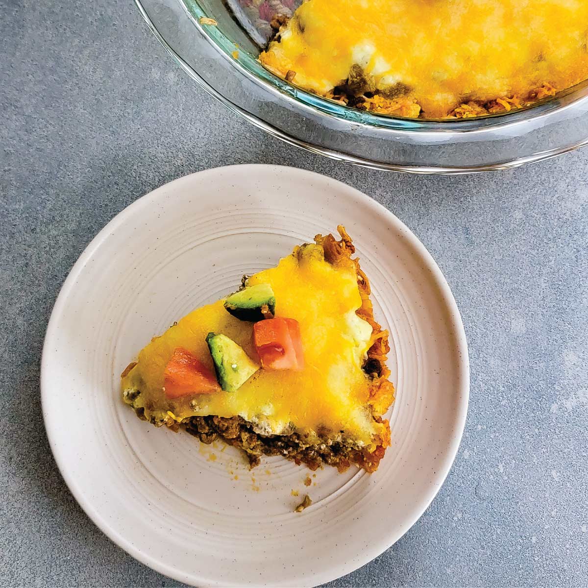 Slice of taco pie on a serving plate topped with avocado and tomato chunks.