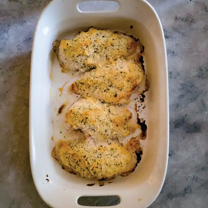 Chicken breasts with parmesan cheese, mayo and breadcrumbs in a baking dish resting before serving.