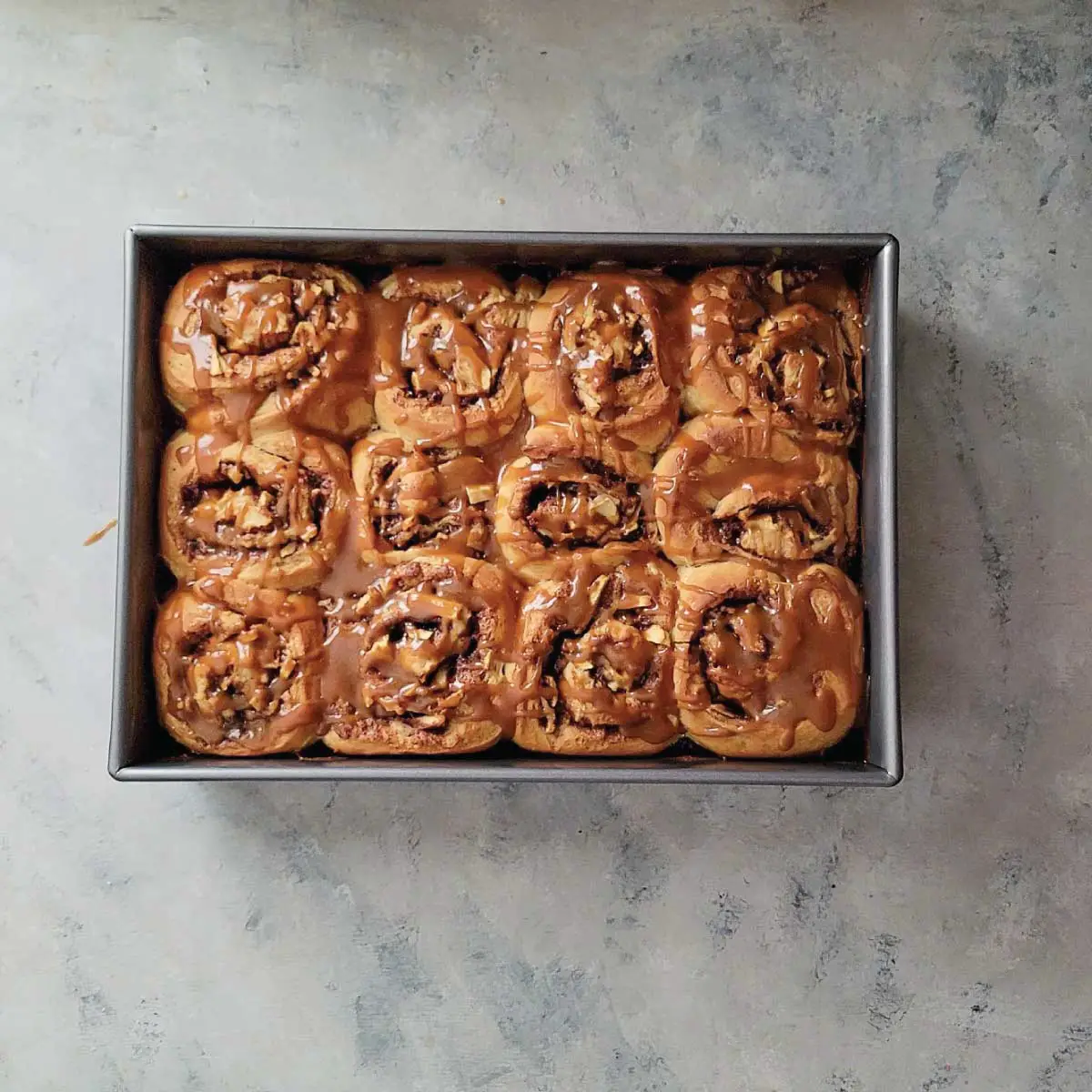 Apple cinnamon rolls in a baking dish with salted caramel drizzled over the top.