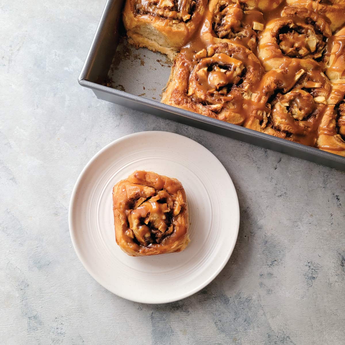 Apple cinnamon rolls with salted caramel drizzled over the top and one roll is on a serving plate ready to eat.