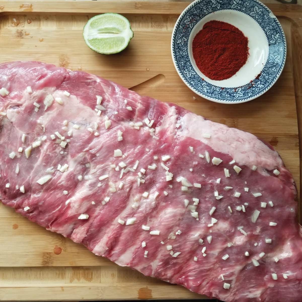 St Louis ribs on a cutting board with garlic, lime and a dry rub prepping for the grill.