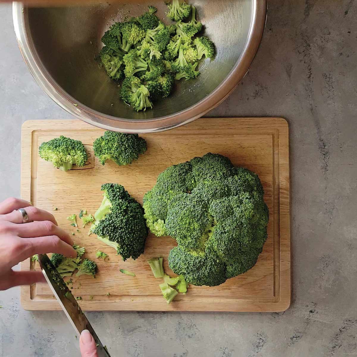 Broccoli being cut into small pieces on a cutting board.
