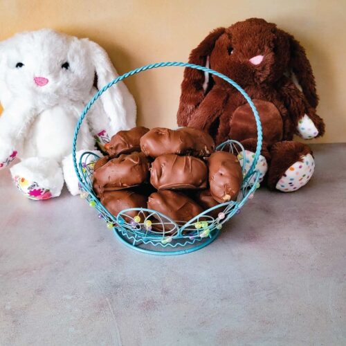 Peanut butter eggs in an Easter basket with 2 stuffed bunnies behind it for decoration.