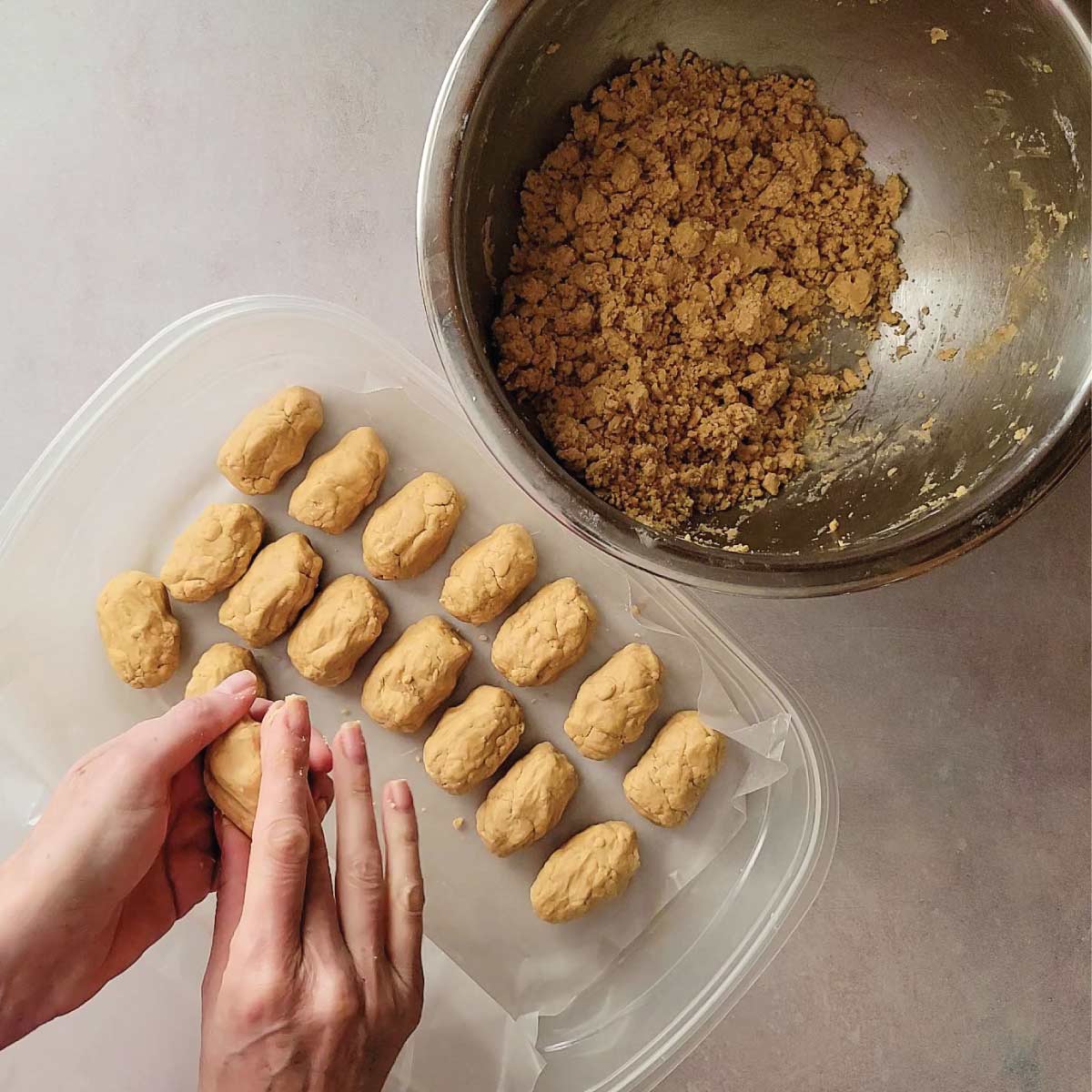 Shaping the peanut butter mixture with hands into the shape of an egg with a few eggs already shaped on wax paper in a container.