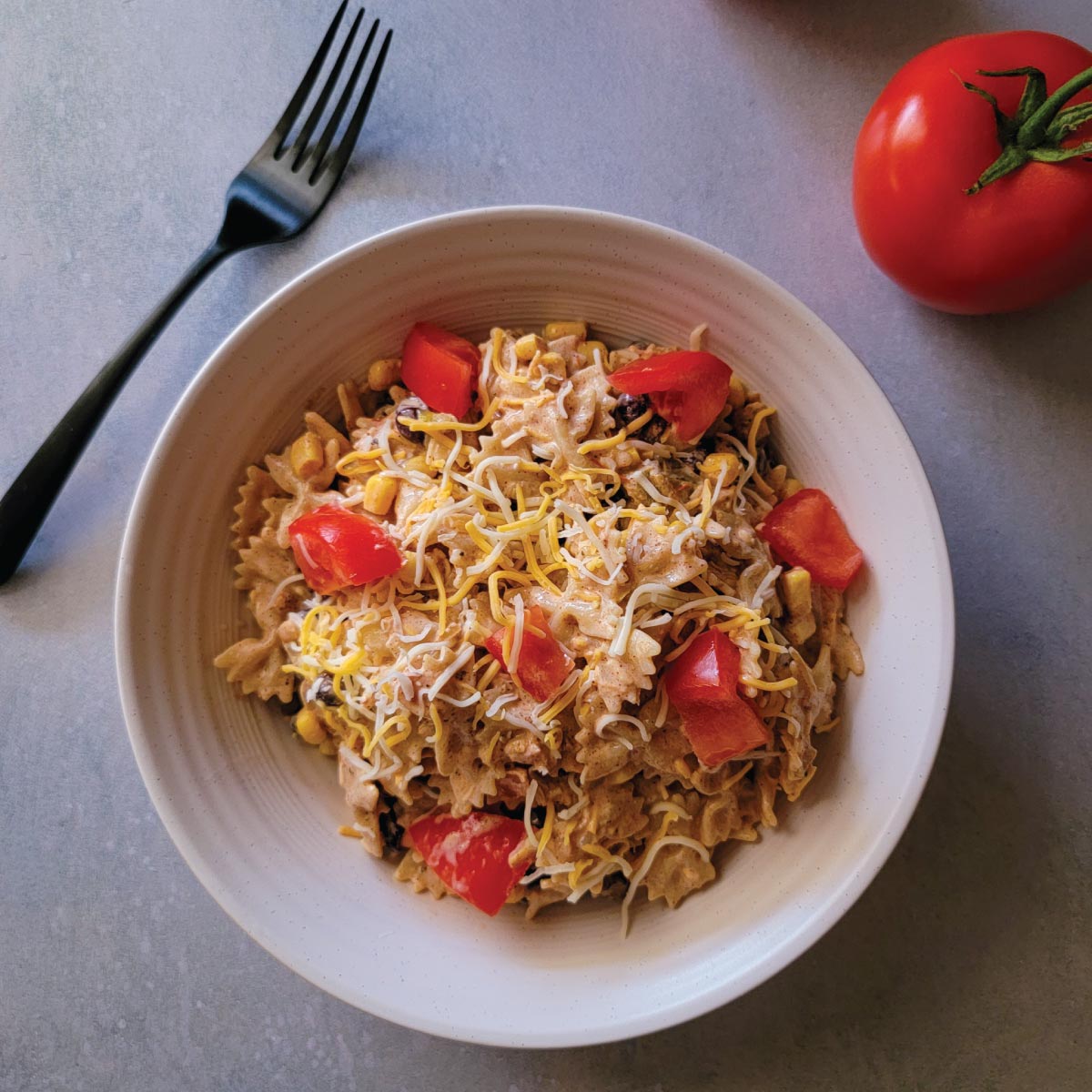 Taco pasta salad in a serving bowl with cheese and diced tomatoes on top for a garnish.
