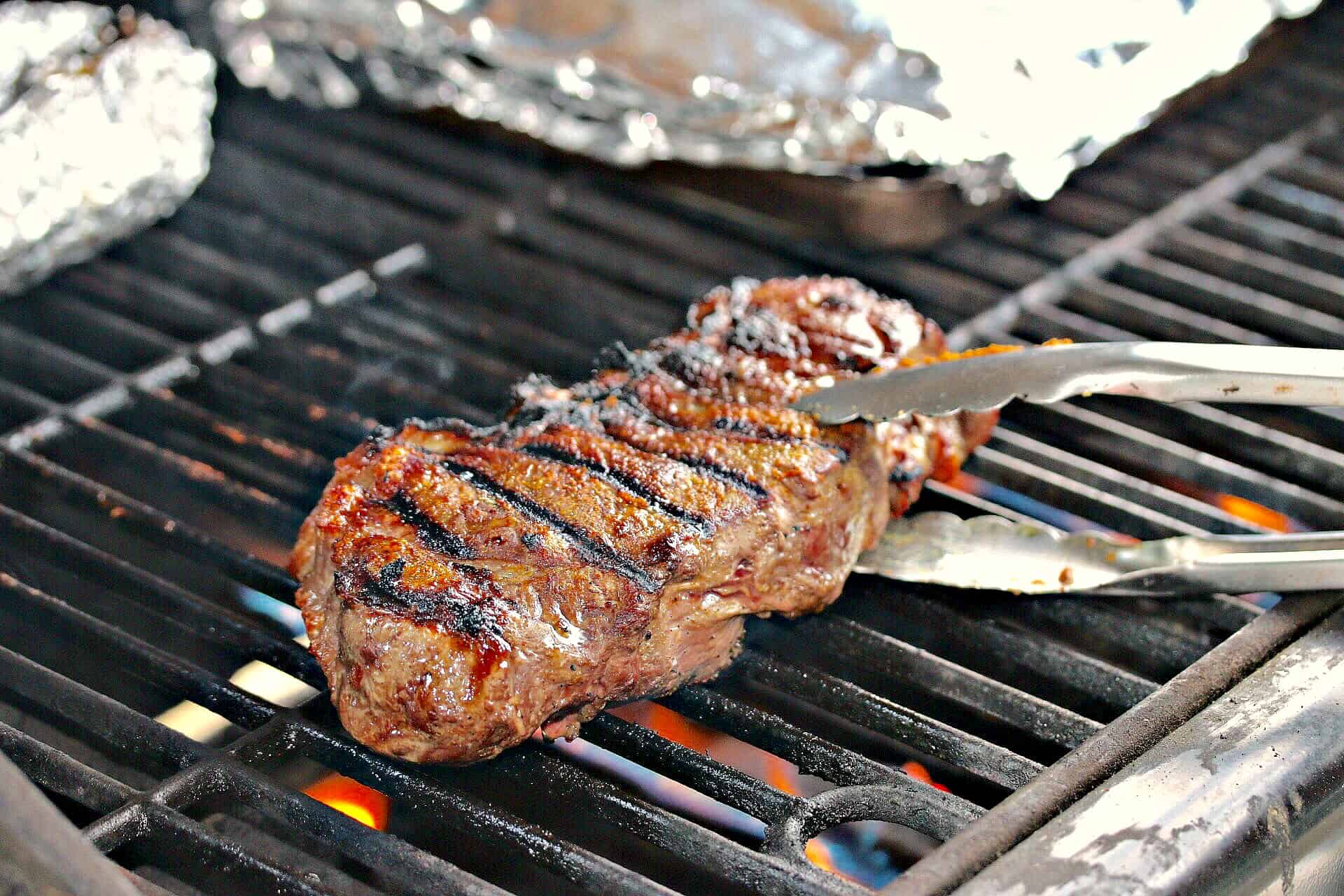 Steak on a grill being moved with tongs.