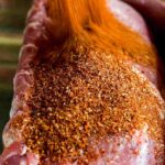 BBQ rub being poured over a piece of meat.