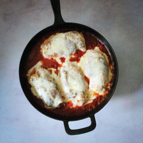 Breaded chicken in sauce in a cast iron skillet topped with melted mozzarella cheese.