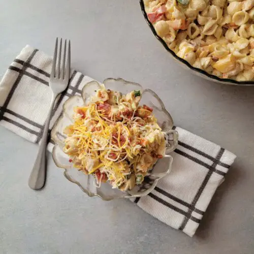 Pasta salad in a serving dish topped with cheese and bacon ready to eat.