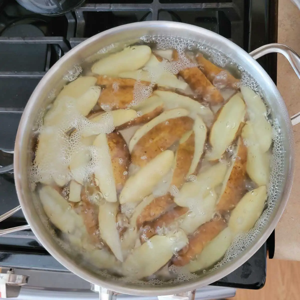 Potatoes cut into wedges and in a large frying pan with water cooking.