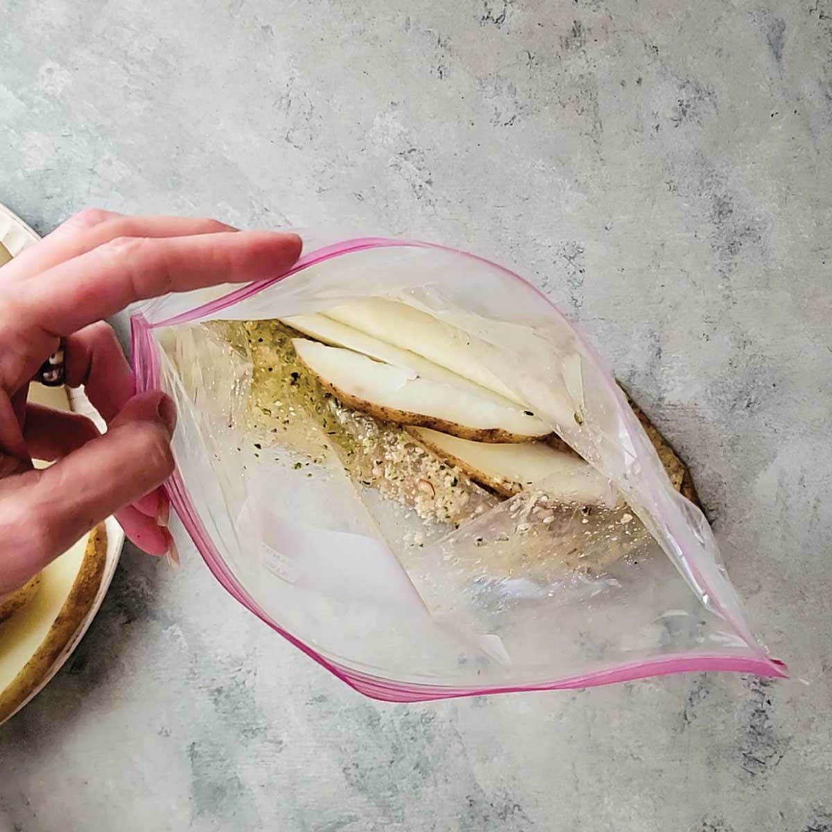 Potatoes being placed in a plastic bag that has oil and seasoning mix in it to coat them.