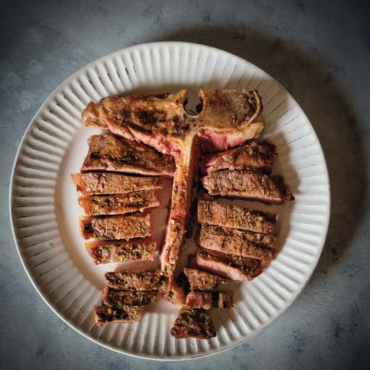Tbone steak on a plate after being cut off the bone and into slices, ready to serve.