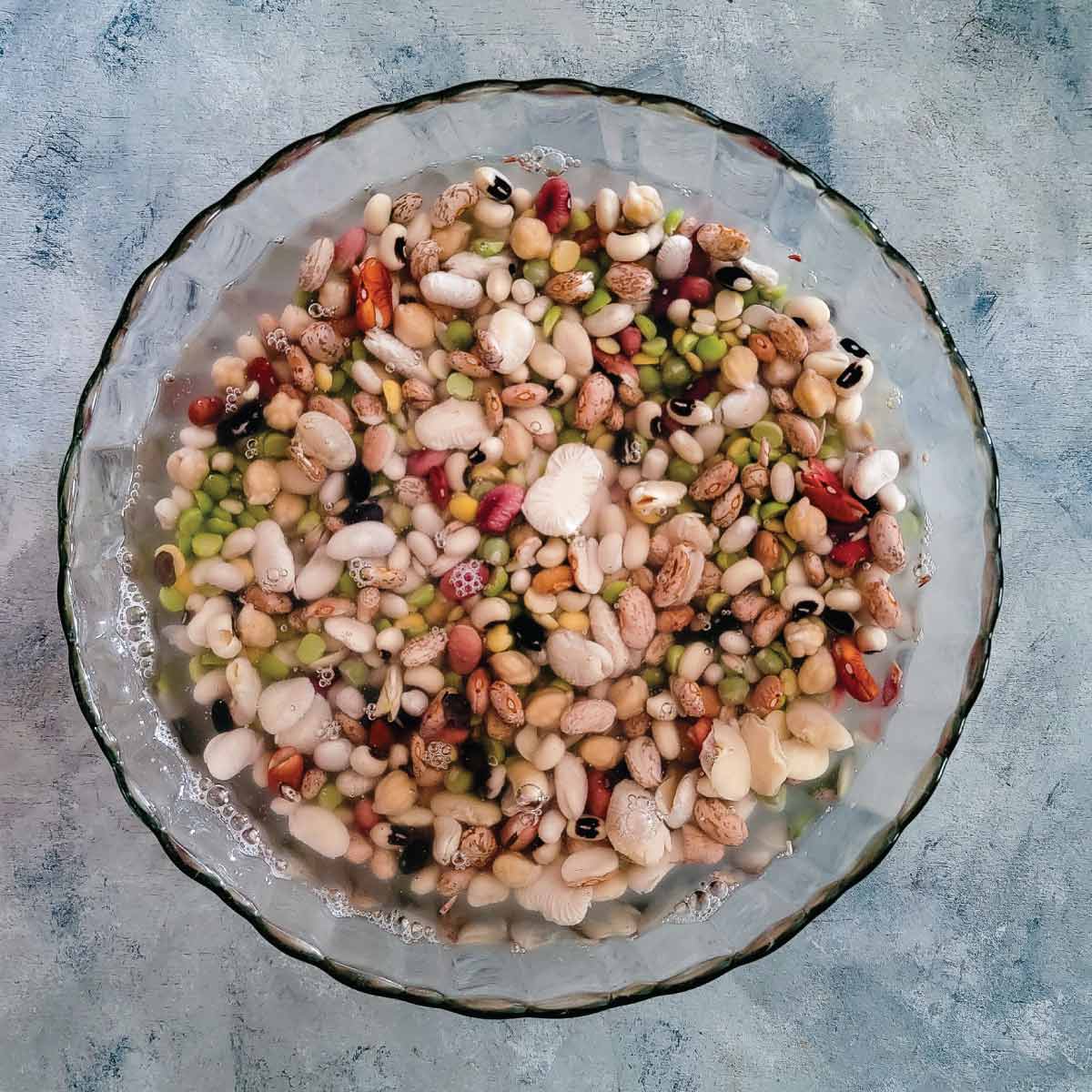 16 bean soup mix sitting in a bowl of water soaking.