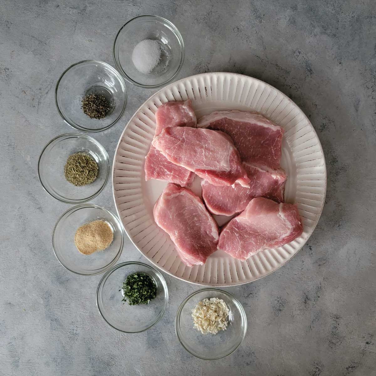 Pork chops on a plate with spices in small prep bowls around them.