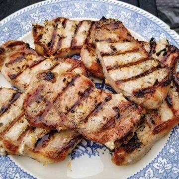 Grilled pork chops resting on plate after cooking before serving.
