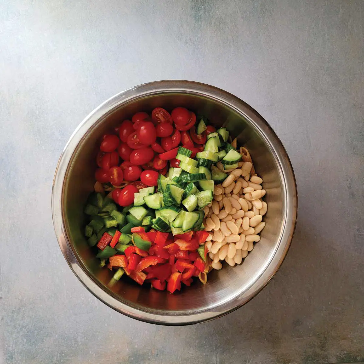 Lentil pasta with cannellini beans, chopped bell peppers, chopped cucumbers and halved grape tomatoes on top ready to mix together.