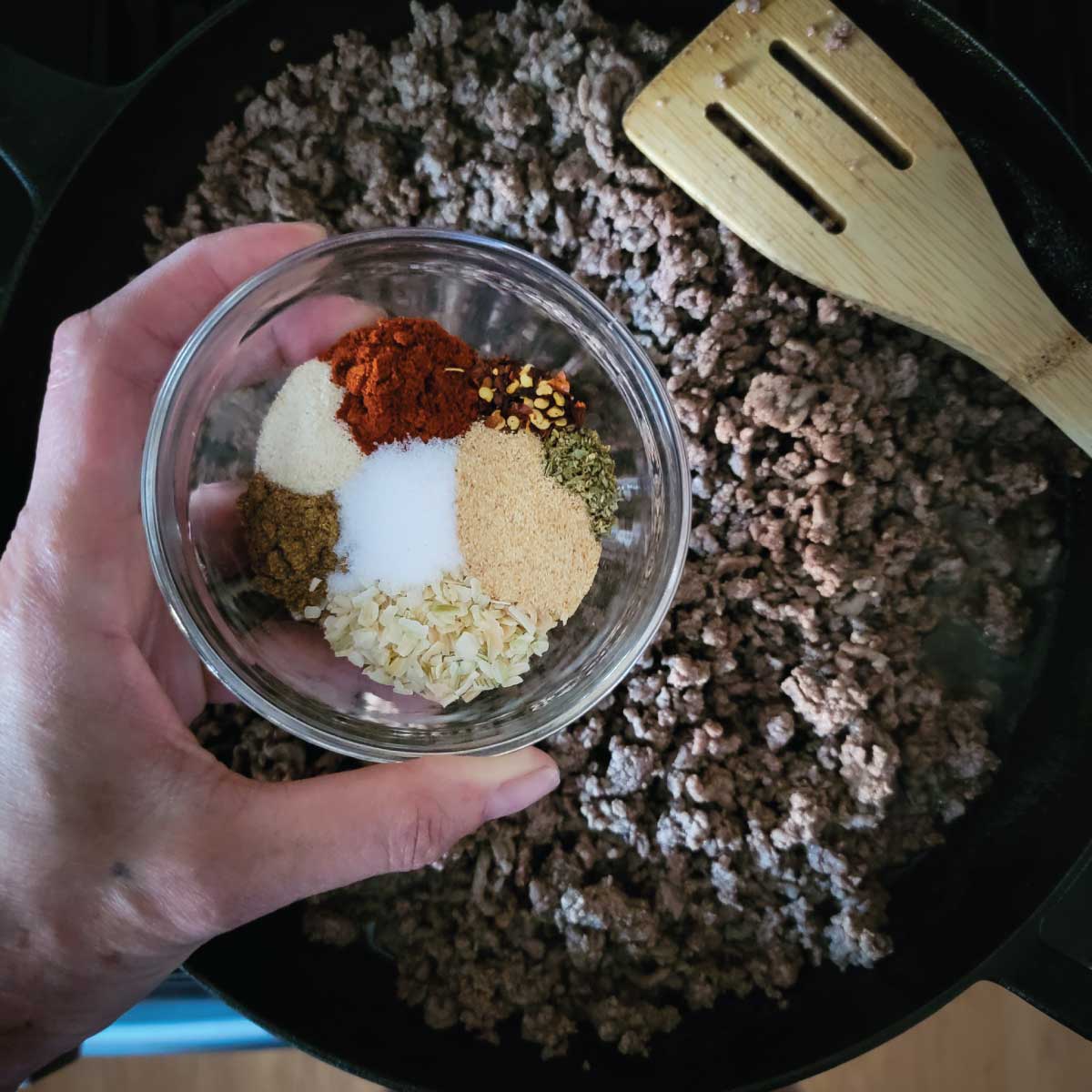 Browned ground beef in a frying pan and the seasoning in a small prep bowl ready to add into the beef.