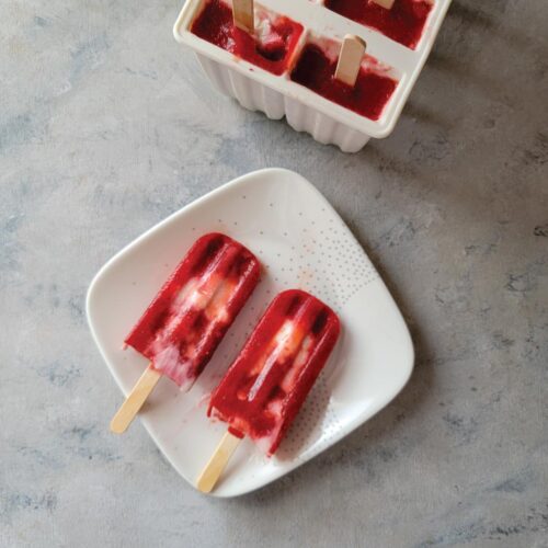 2 popsicles with berries and yogurt out of the mold and on a plate ready to eat.