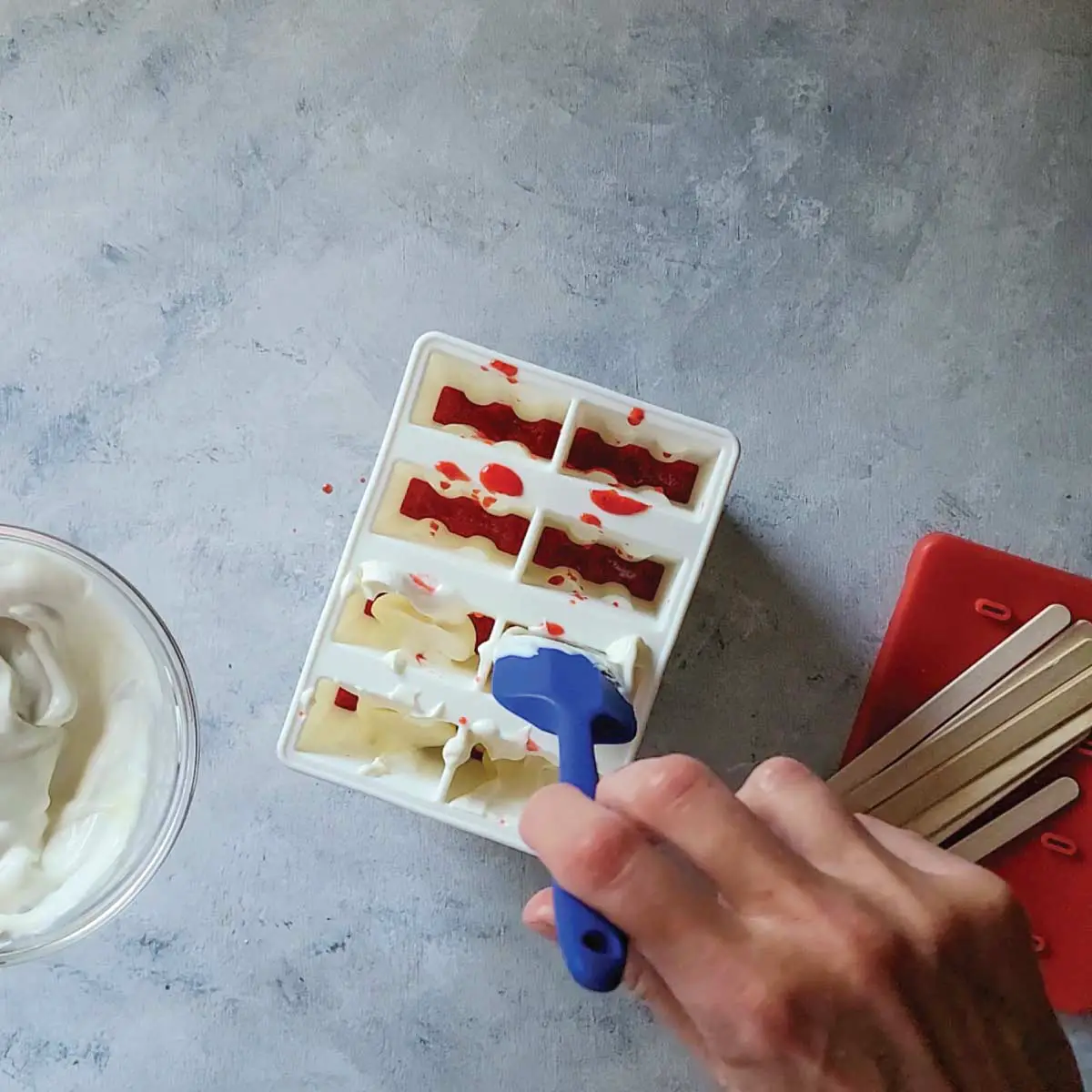 Adding a layer of yogurt on top of the strawberry puree in the silicone popsicle mold.
